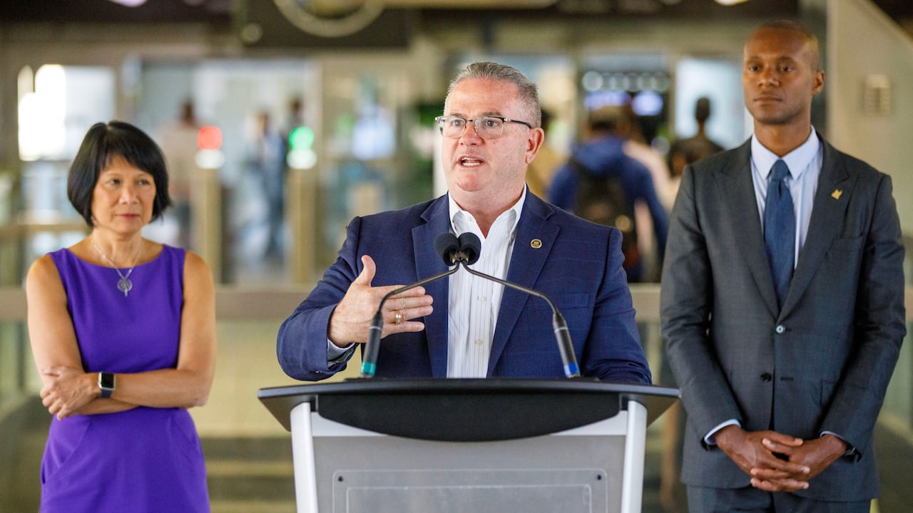 A transit executive speaks at a lectern in a transit station.