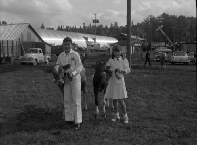 Two children hold cows in a black-and-white image and smile at a fairground.
