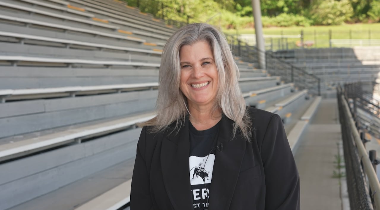 A white woman with silver hair smiles in an empty grandstand.
