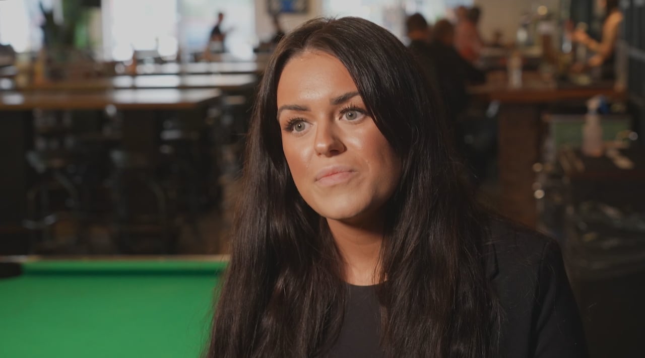 A woman with long black hair is seen in a bar.
