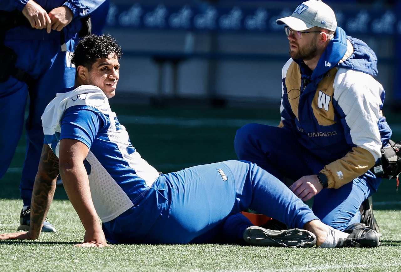 A football player in blue and white sits on the turf with his helmet off.