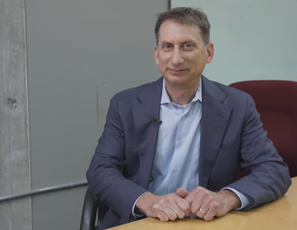Man in suit and button-up sitting at table, looking at camera
