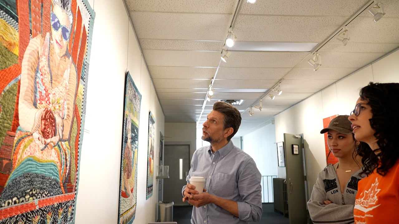 Man and two women look at paintings.