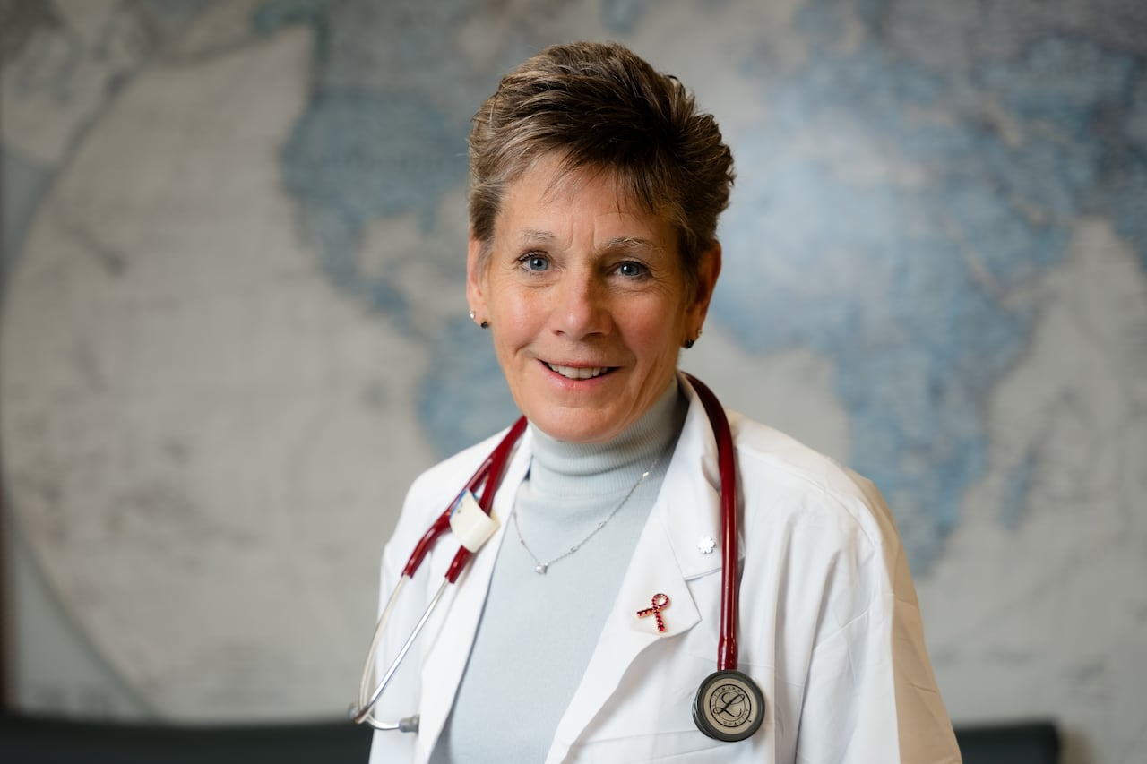 Woman in doctor's coat, with stethoscope draped around her shoulders stands with a map of the earth in the background.