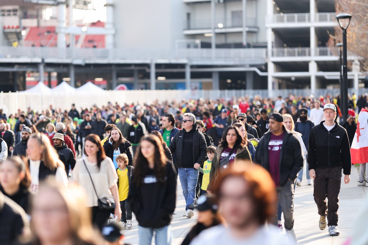 A large crowd of people in a parking lot all walk toward the camera.