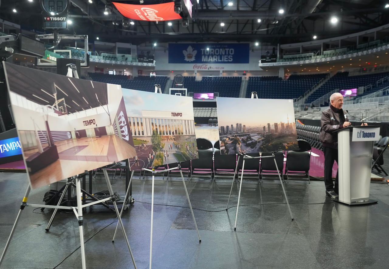 At the right, a man stands at a podium in an empty arena. At left there are three different artist renderings of building facilities on display.