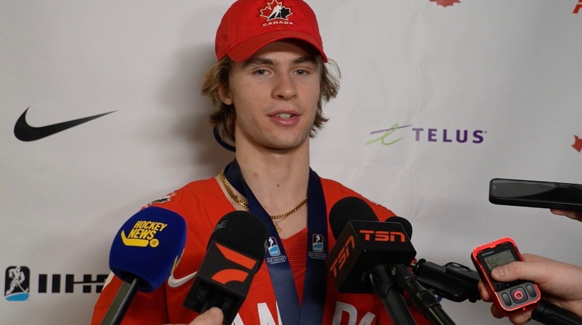 A young man in a Canada hat and jersey is scrummed by reporters.