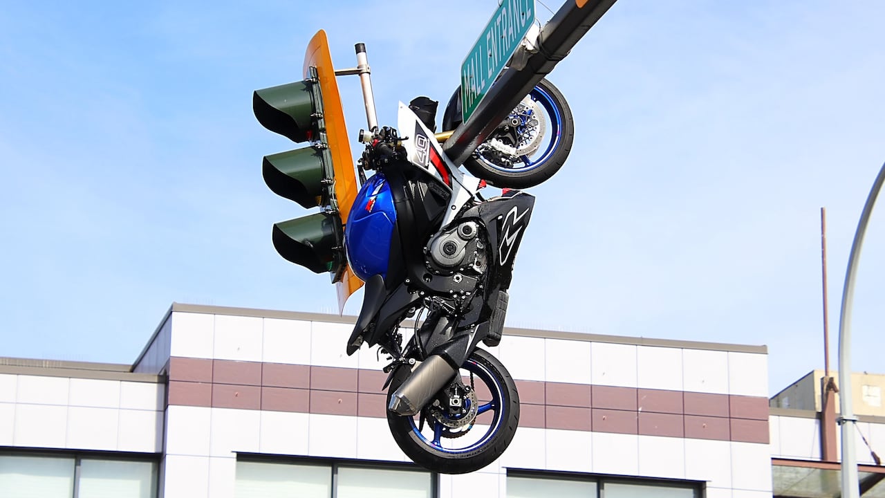 A motorcycle is lodged on an overhead traffic light above an intersection