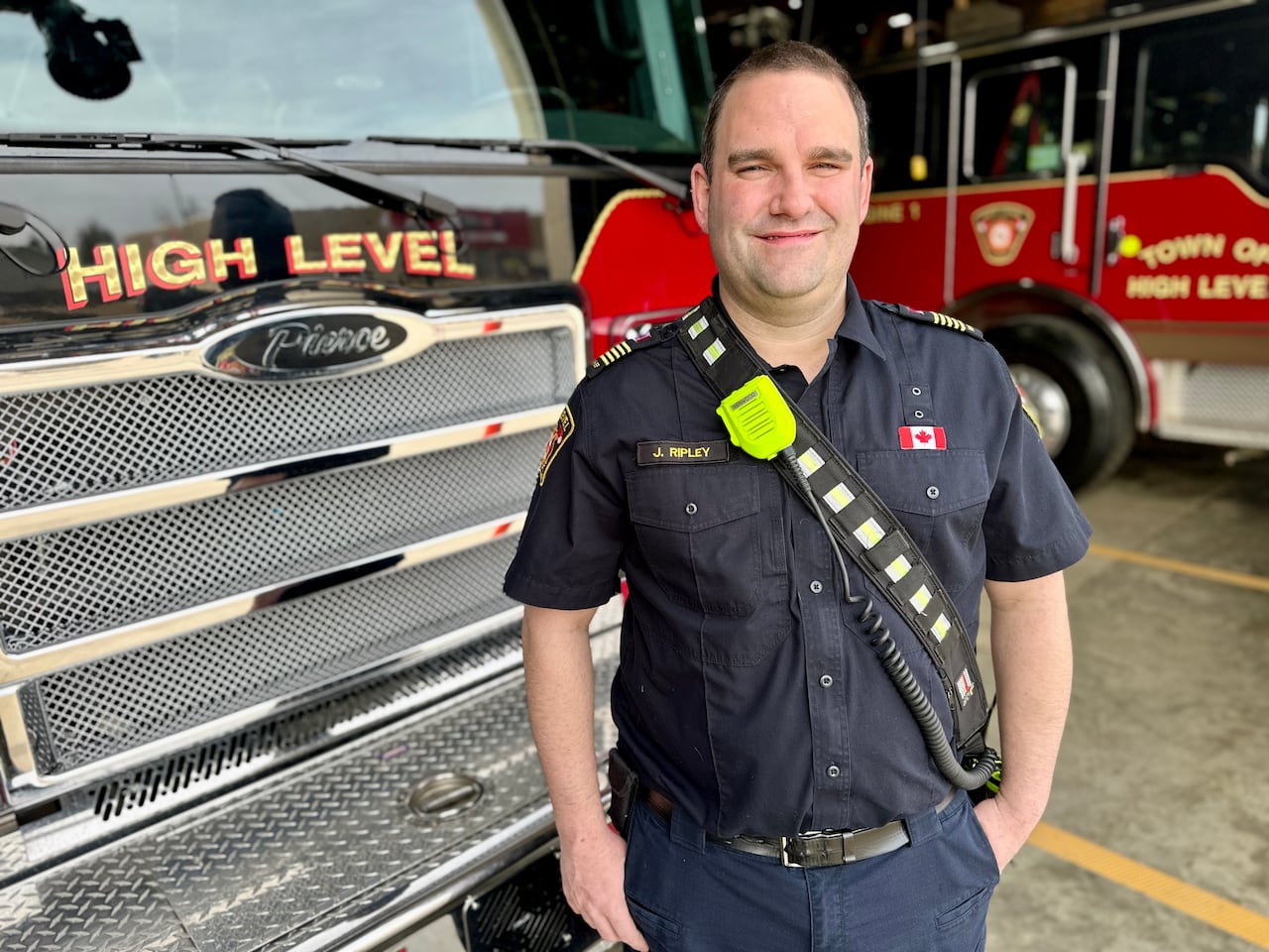 A man in a blue shirt and blue pants stands in front of some shining fire trucks.