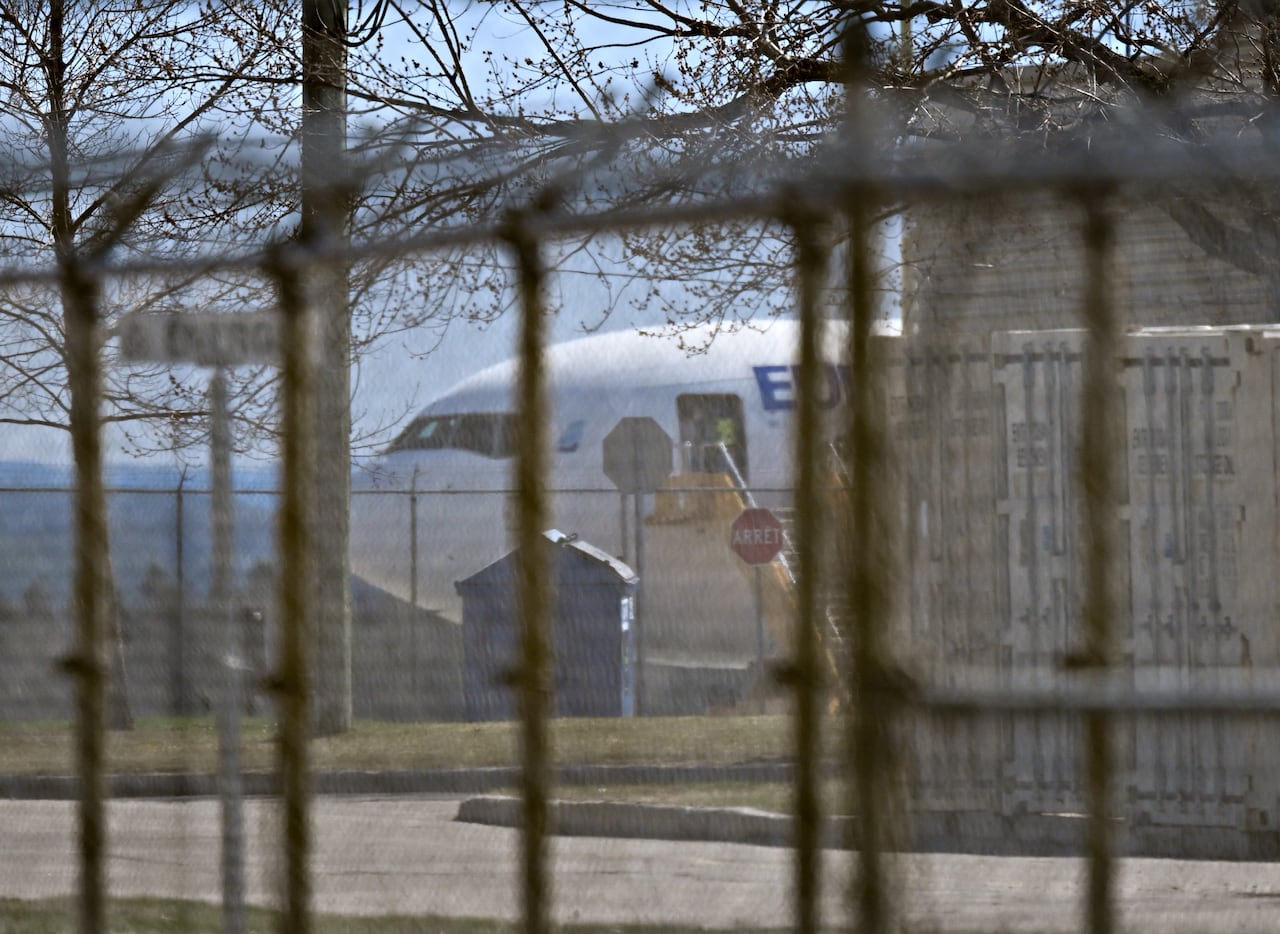 The front section of an airplane is seen as photographed through a a fence on a sunny winter day.
