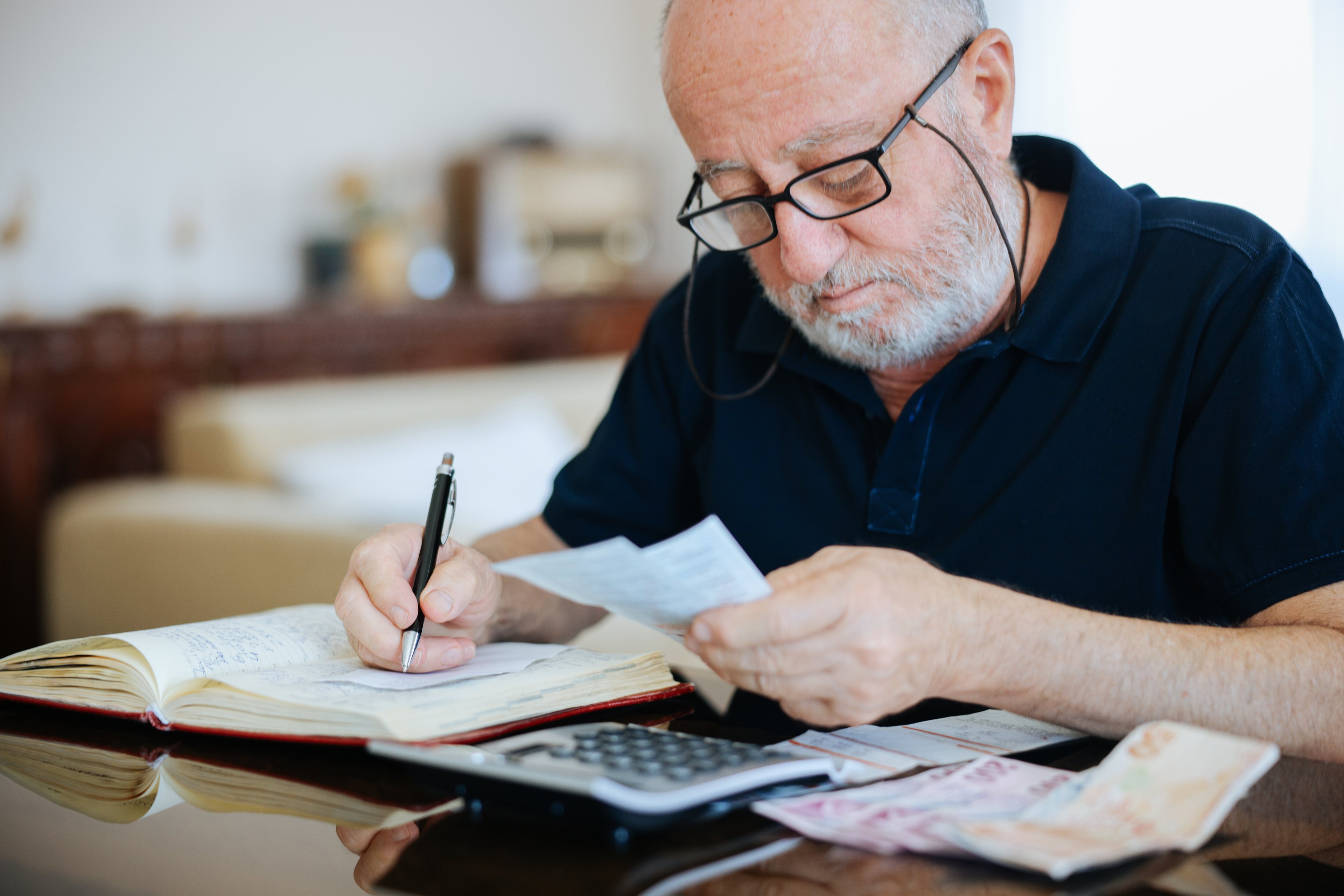 Someone looking at a paper while writing in a book.