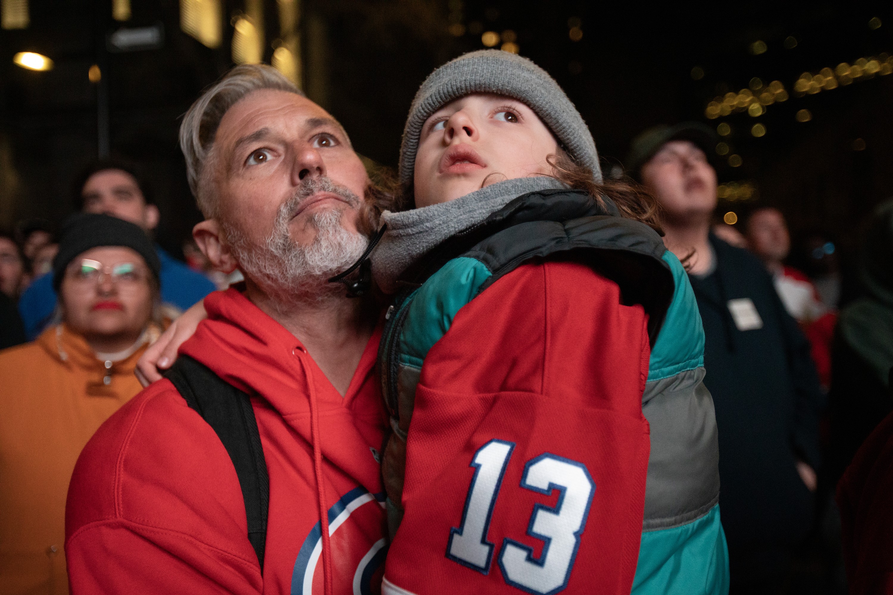 A man holds his son as both stare intently at an unseen screen.
