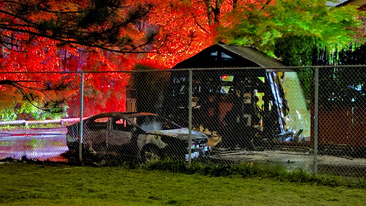 A torched vehicle is seen next to a small garage in an alley.