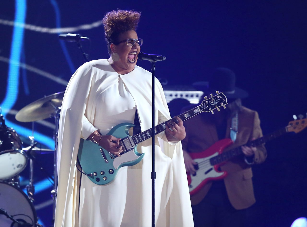 A black woman holding a blue guitar sings on stage.