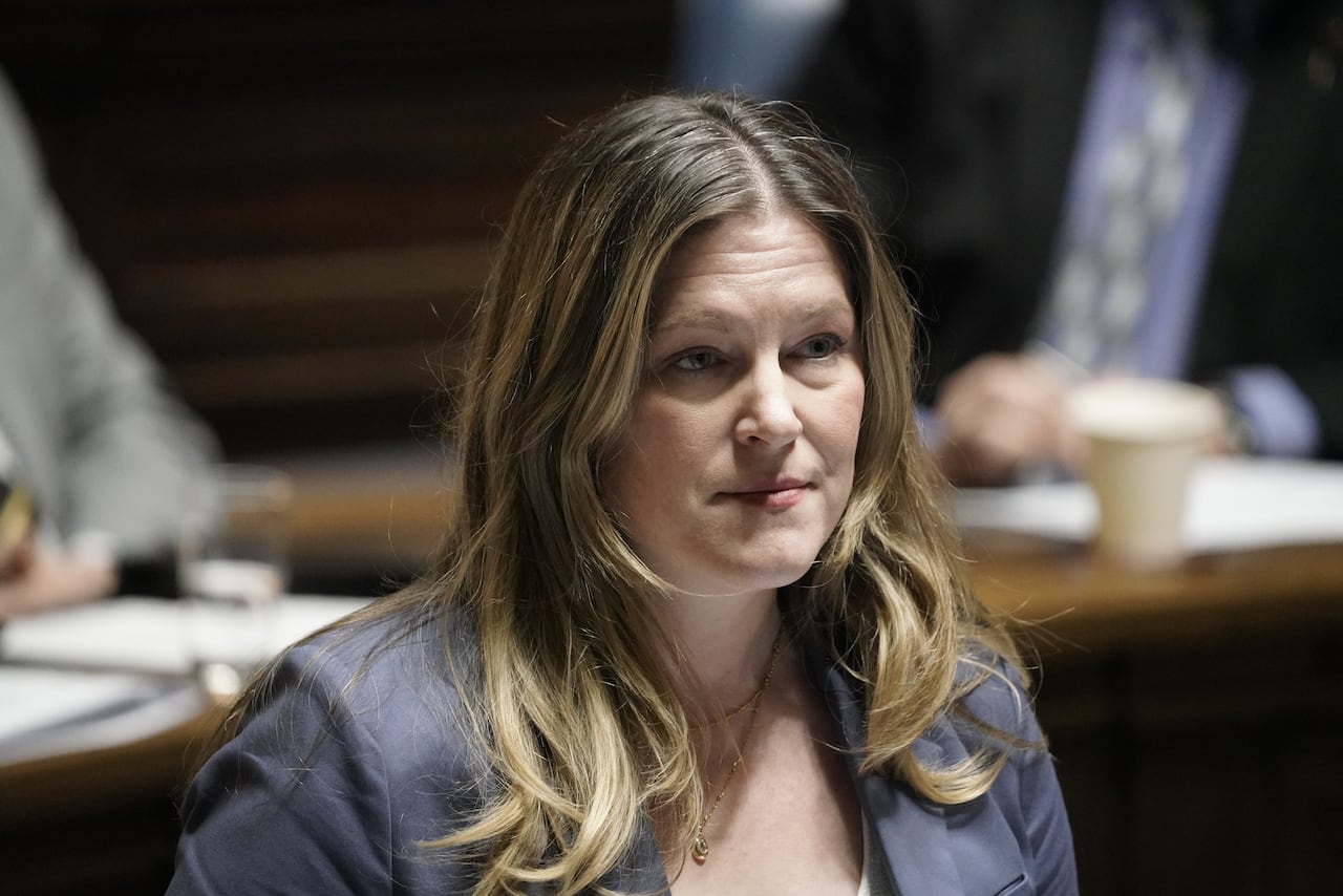 A woman with long blond hair wearing a bluish blazer speaks during a government legislative session.