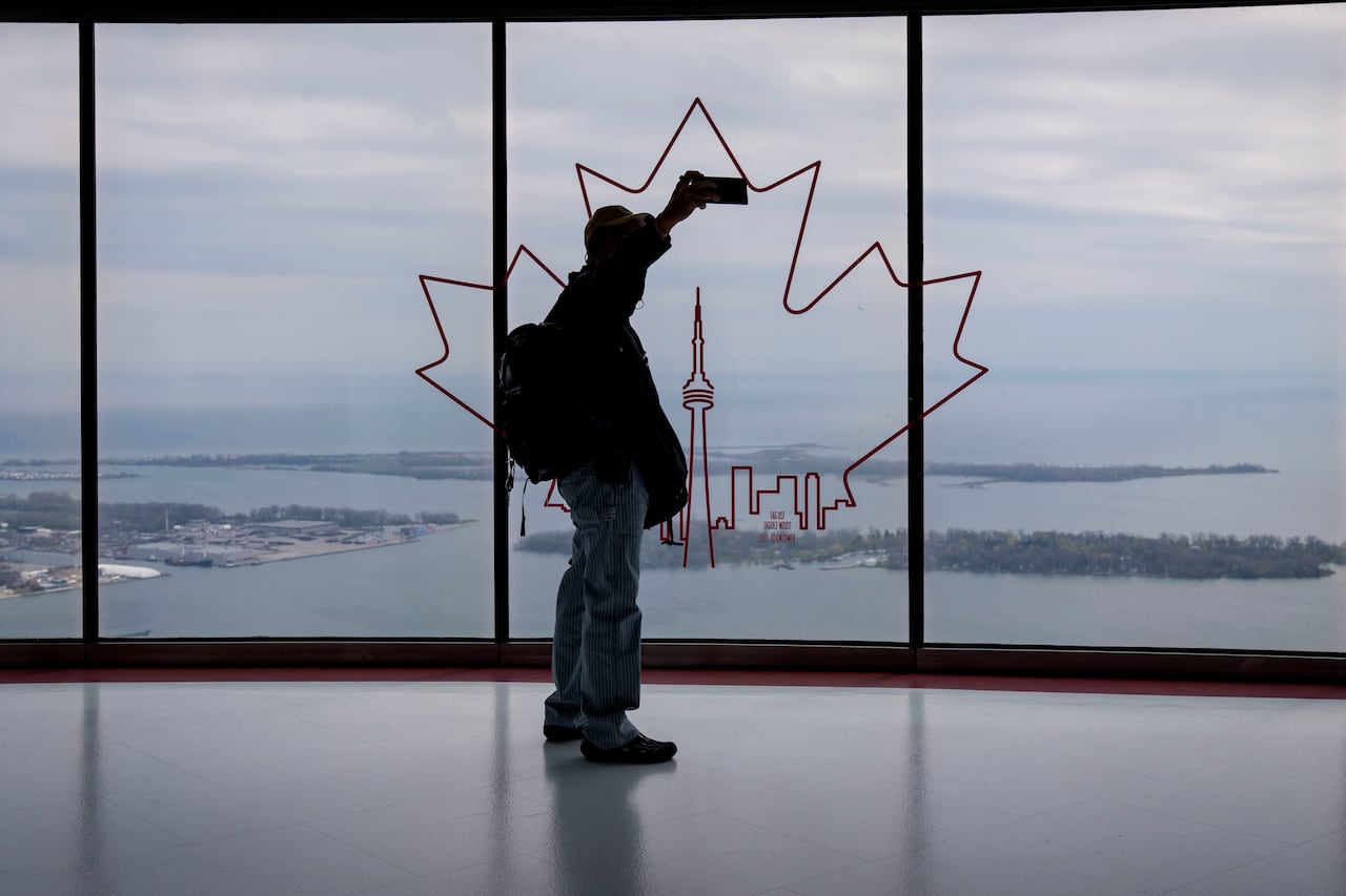 A person taking a selfie on an observation deck of the CN Tower with backdrop of Lake Ontario.