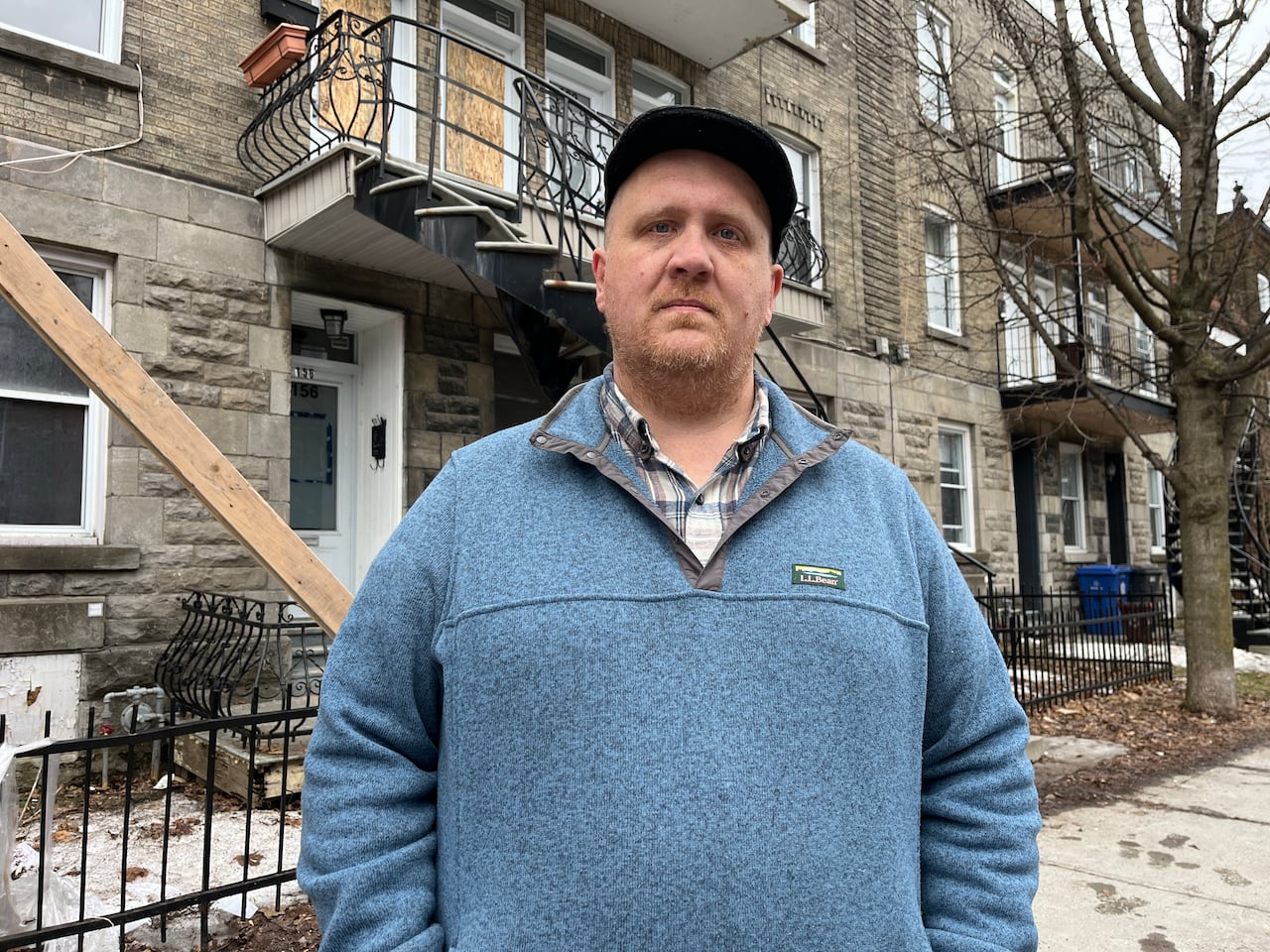 Photo of a man standing in front of a boarded up building.