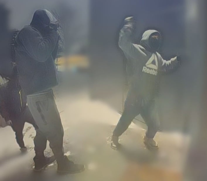 A masked man raises his arm to smash the window of a house with a hammer.