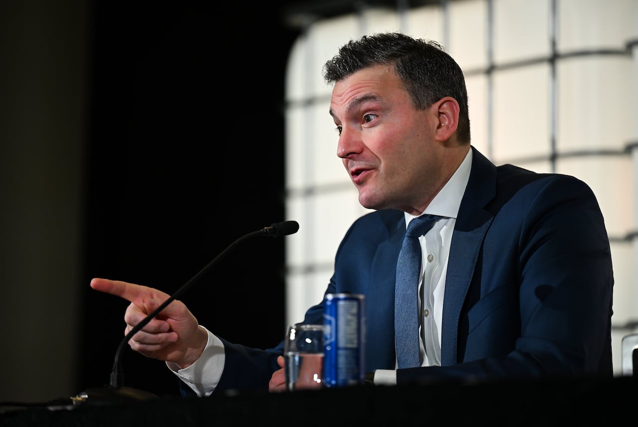 A politician points with a finger as he answers a question from a journalist while sitting on stage in front of a microphone.