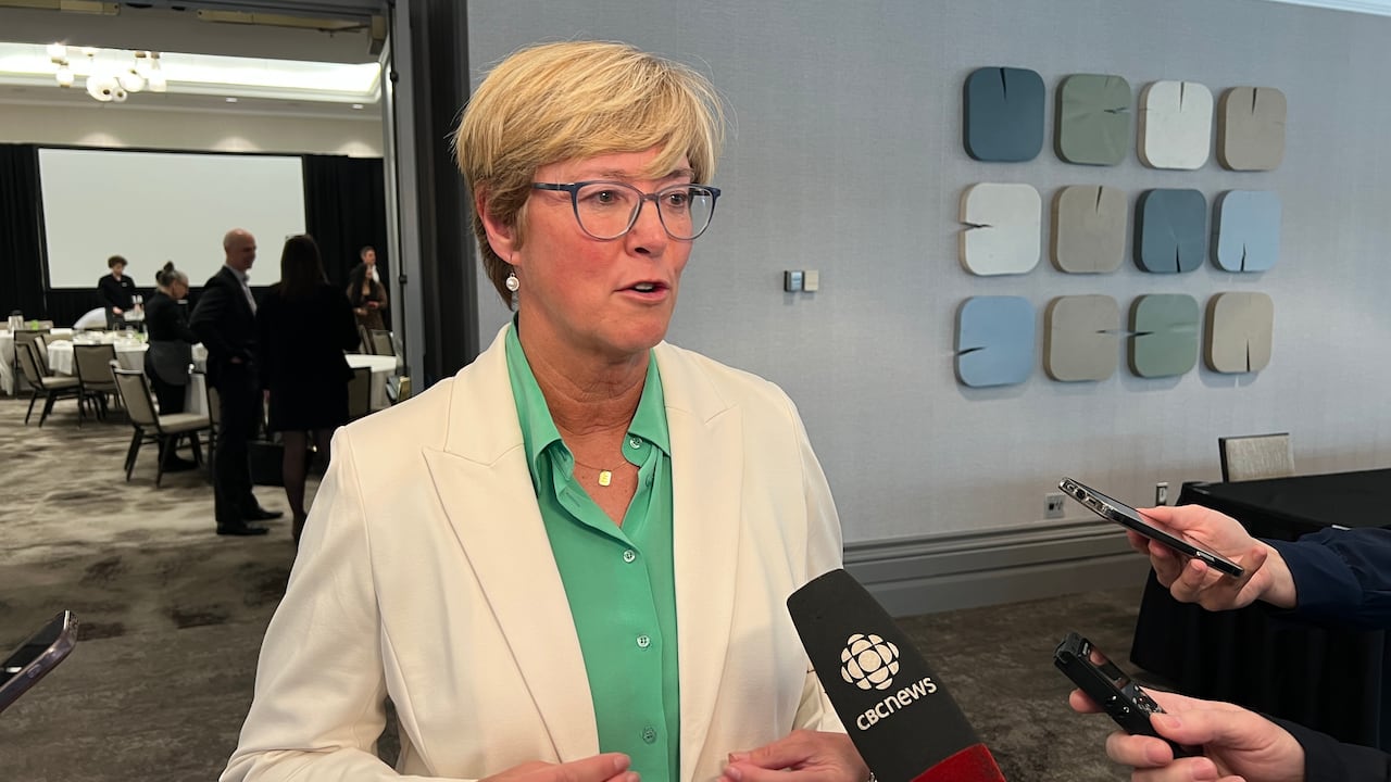 A women with glasses stands in front of microphones.