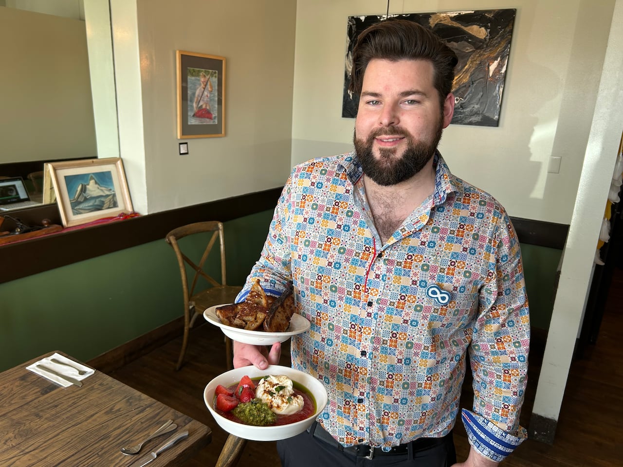 A smiling man holds two plates of food inside a restaurant.