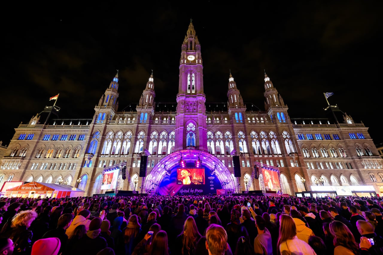 Lots of people gathered outside Vienna city hall at nighttime.