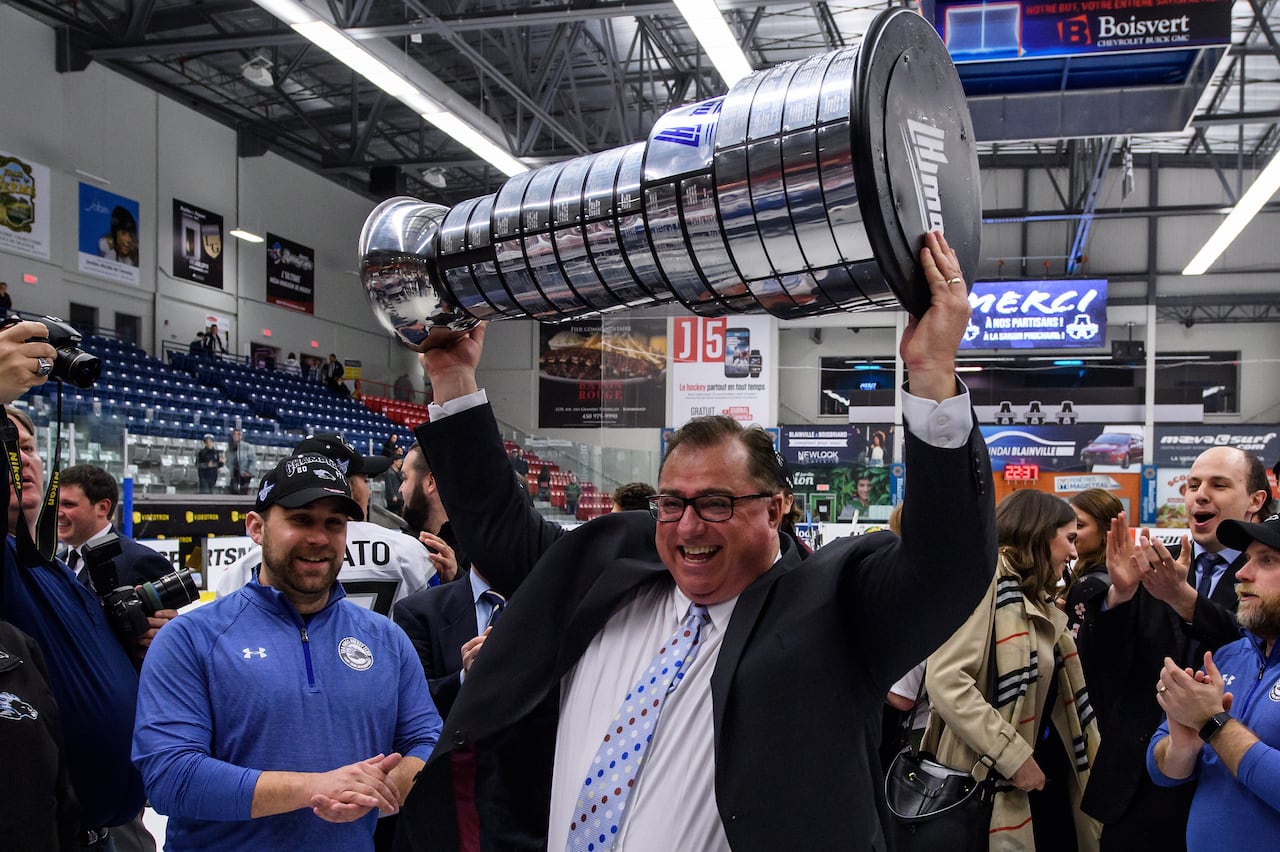 A man wearing a suit and tie holds a hockey trophy over his head.