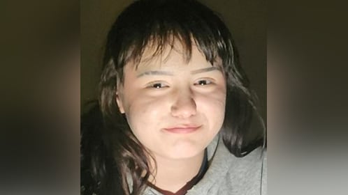 Young girl with dark hair and bangs wears a grey sweater