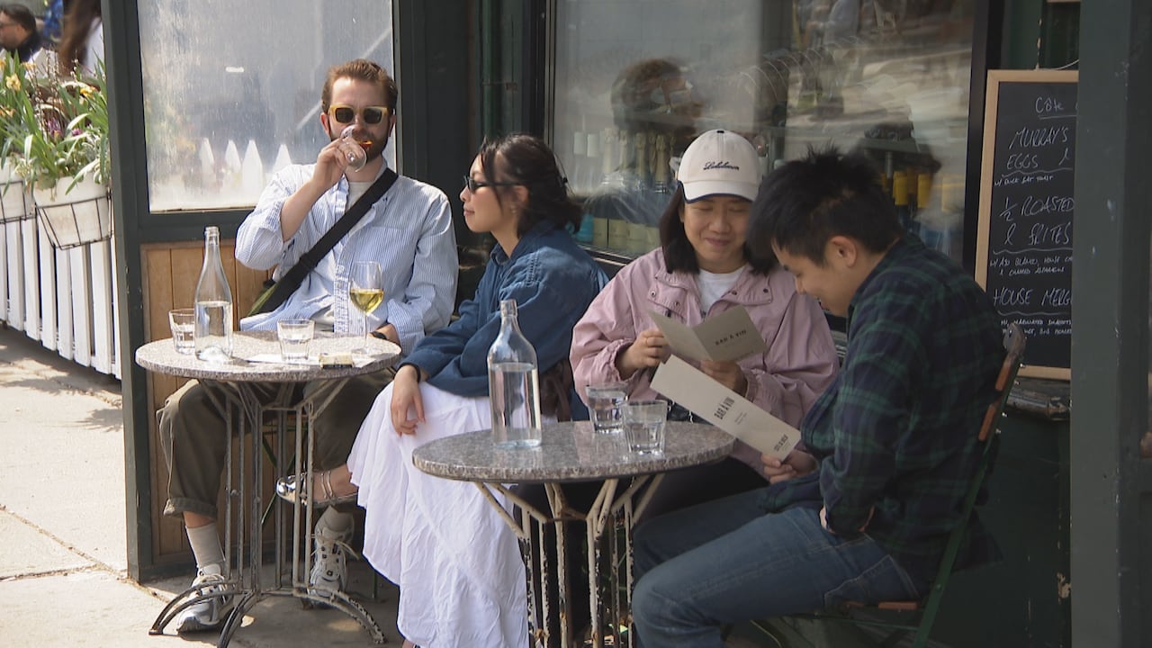 People sitting at little tables in front of store enjoying the weather and drinking