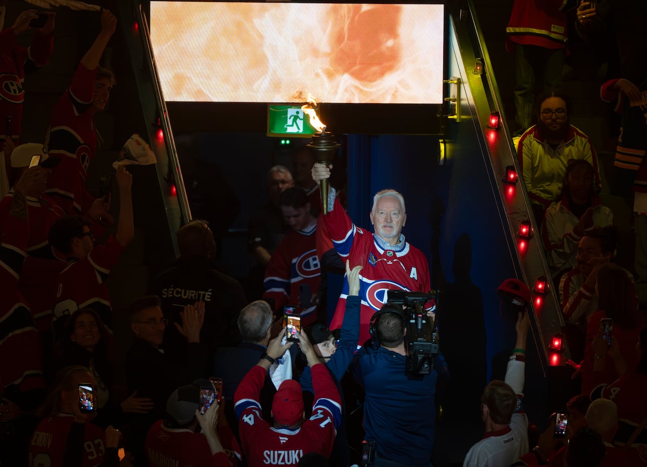 A former hockey player carries a burning torch into a hockey arena prior to a match.