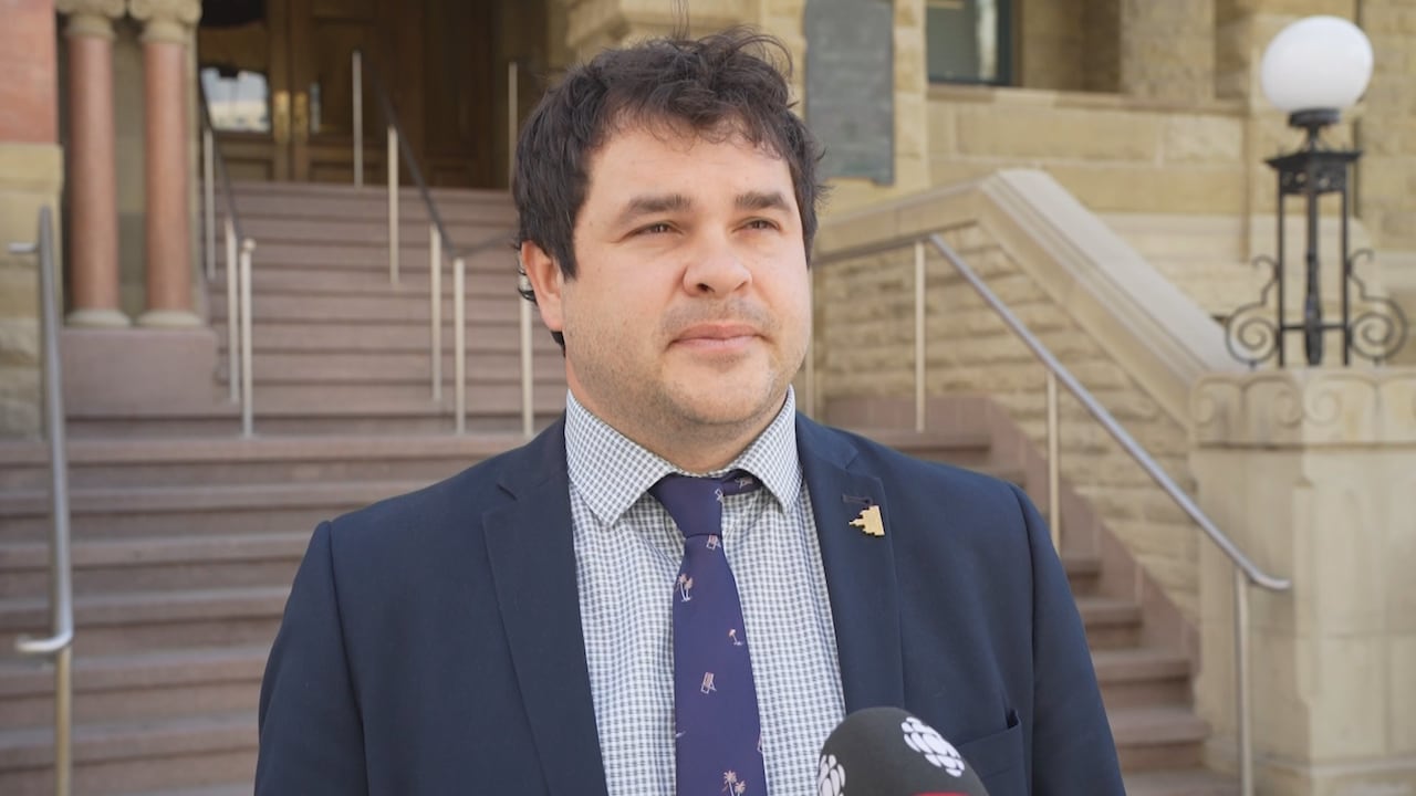 A man in a suit is interviewed in front of a staircase to a building.