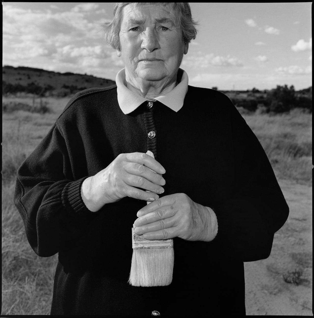 Woman in black holding a paintbrush.