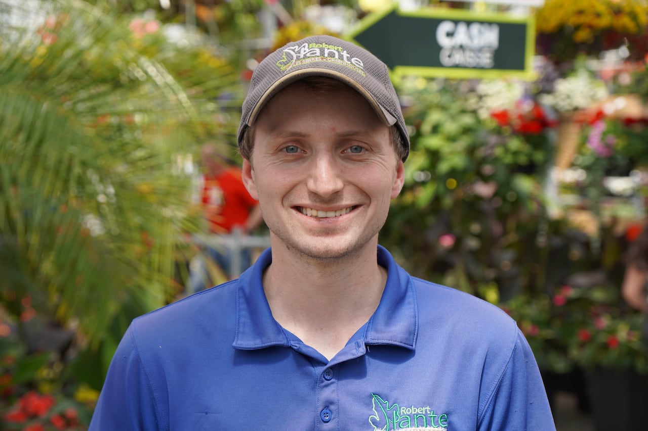 A photo of a man wearing a hat in a greenhouse.