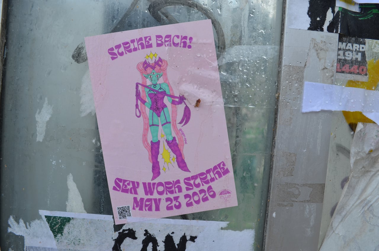 A poster taped to a phone booth. It just rained. The poster reads "Strike back, sex work strike may 23 2026"