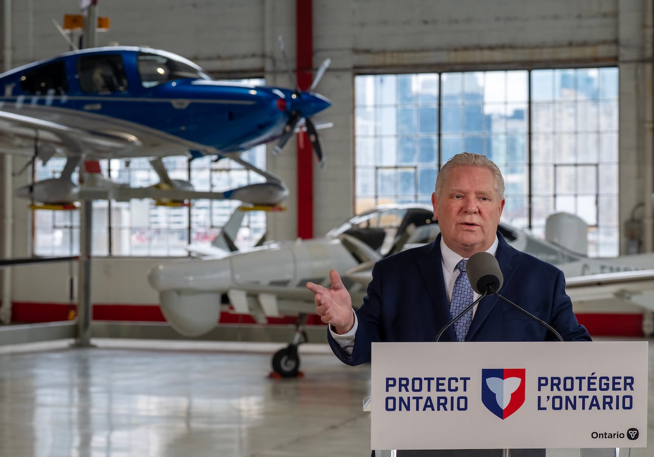 Doug Ford speaks at a podium, with planes behind him.