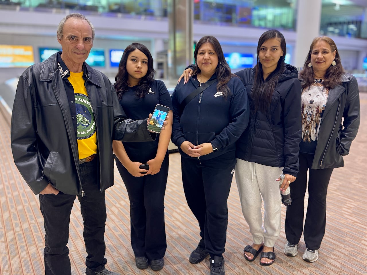 A group of people pose for a photo at an airport, one of them is holding up a photo of a woman.