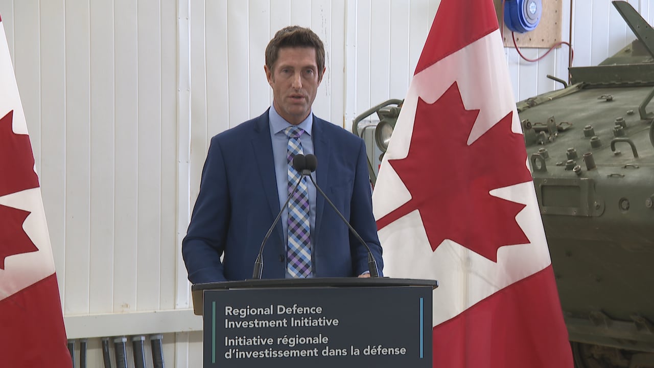 A man in a suit speaking a a podium in front of a Canadia flag