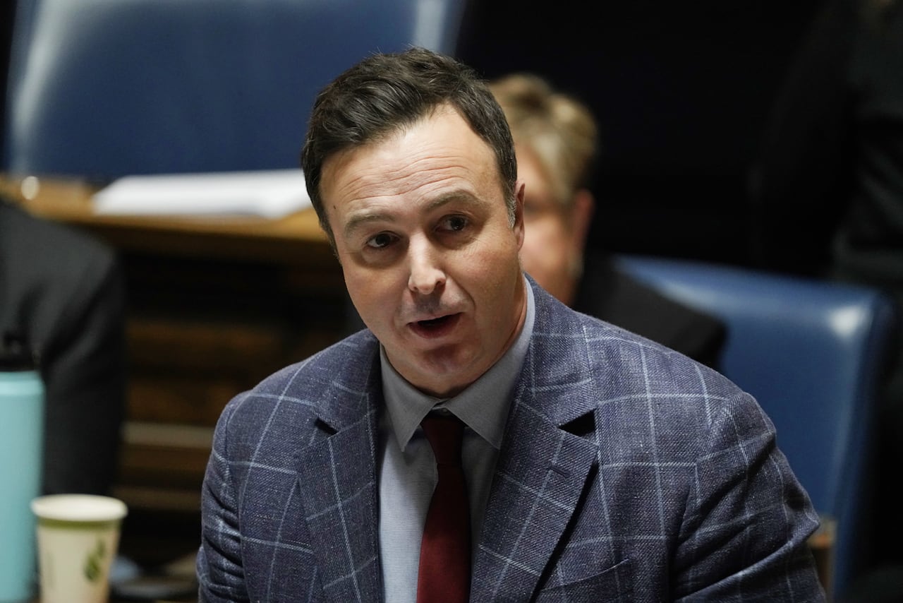 A man in a blue-patterned suit and red tie speaks during a government legislative session.
