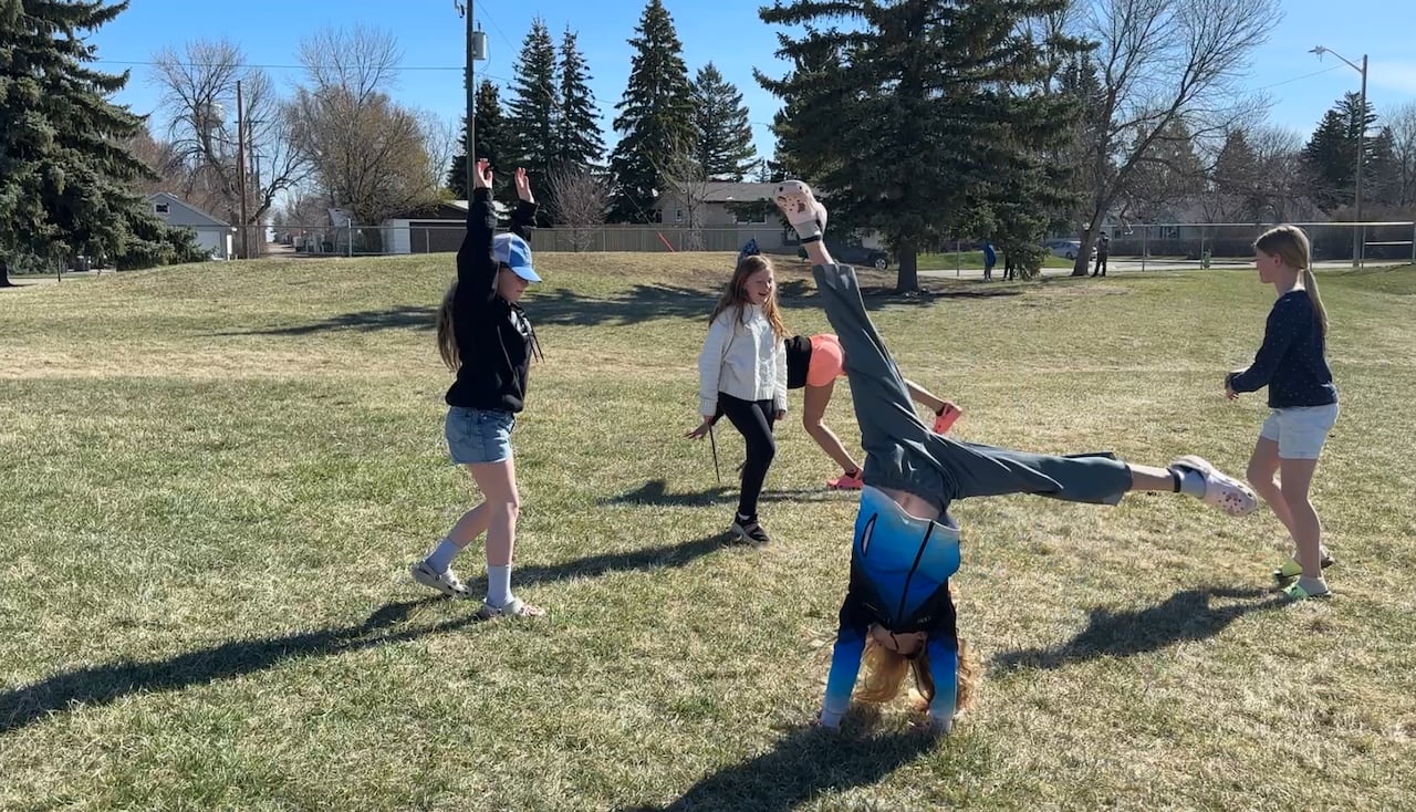 A group of girls do cartwheels in the field.