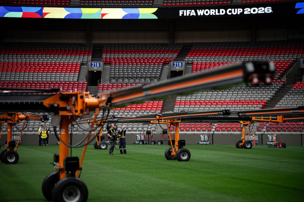 Orange metal machines seen on a green soccer pitch with stadium stands in the background.