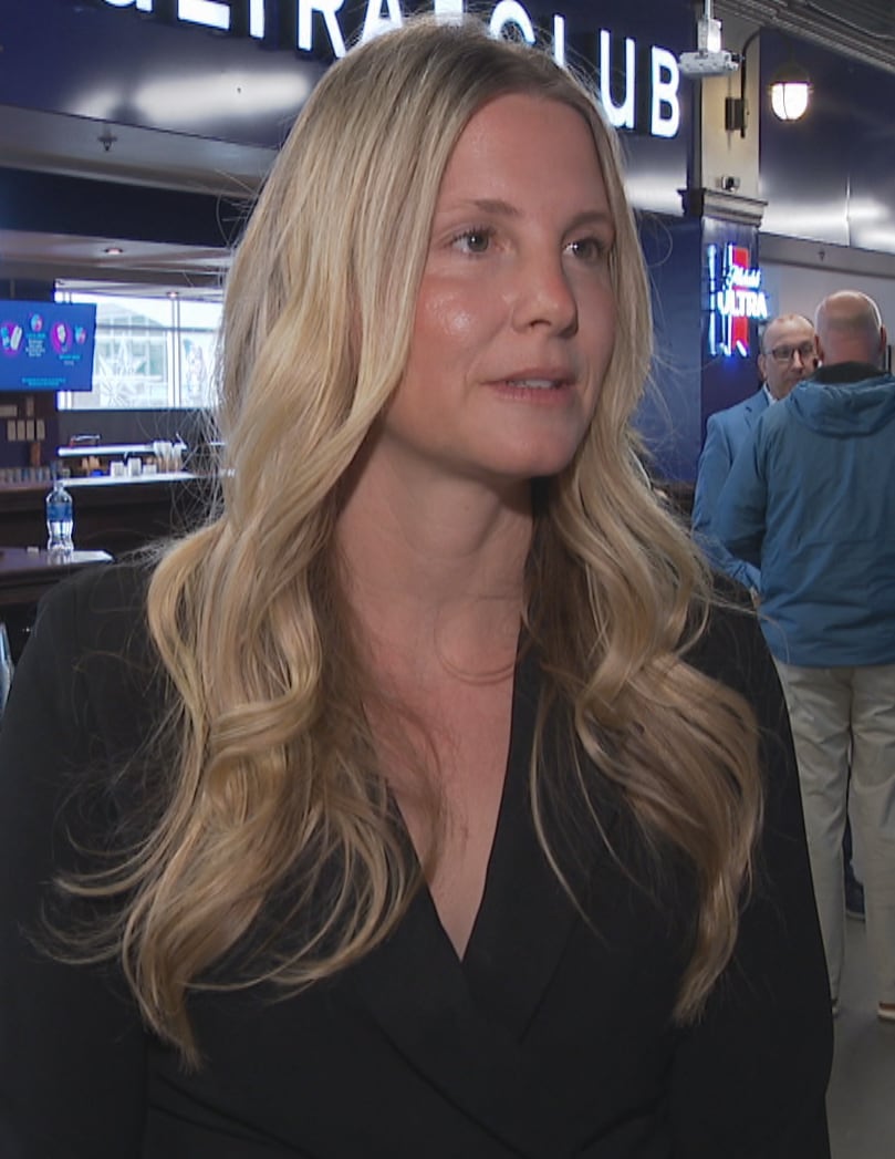 Blonde woman in a hallway, beer signs, people behind her.