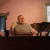 Ken Warner is pictured at his desk, a large computer monitor is visible. His cat is on the desk, looking at the camera.