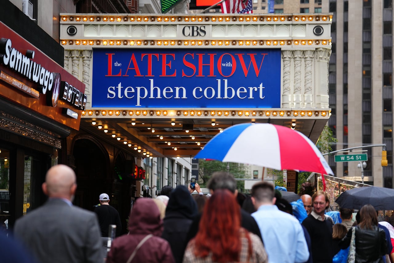 crowd of people waits in a line beneath the sign that says The Late Show with Stephen Colbert at the Ed Sullivan Theatre in New York