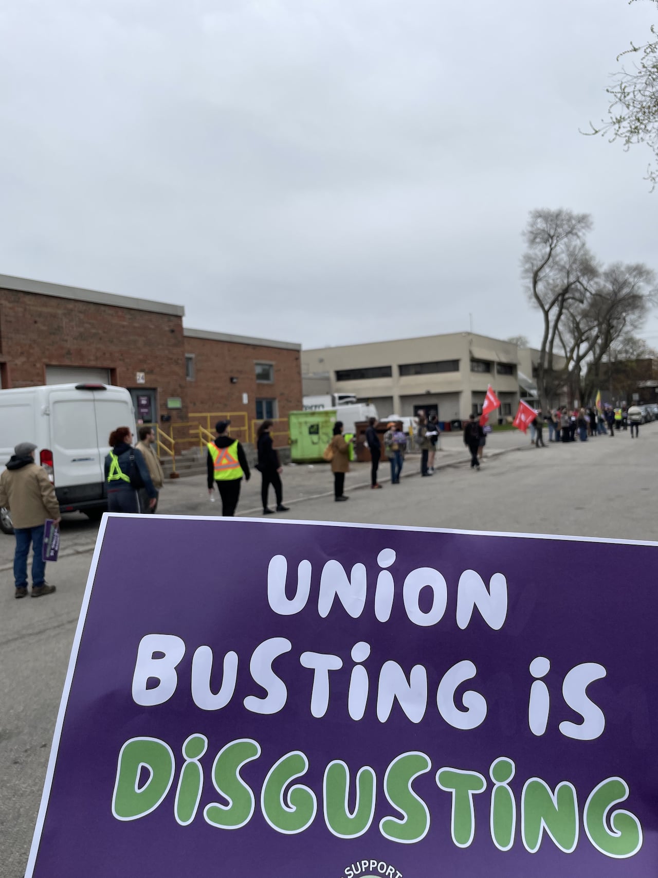 A sign held up reading "union busting is disgusting" with rallying former employees in the background.