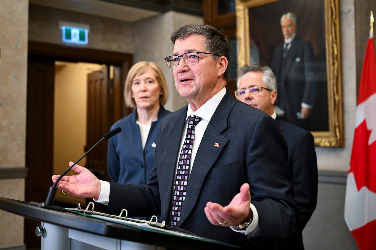 A man in a suit and glasses stands in front of a podium.