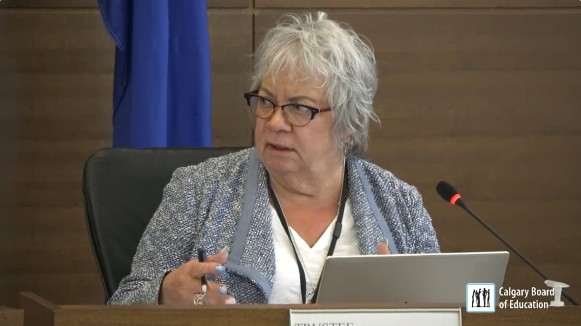 A woman sits at a desk and speaks into a microphone.