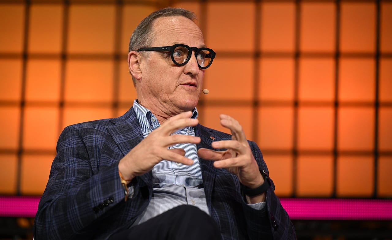 A man in a suit gestures with his hands while speaking on stage at a conference.