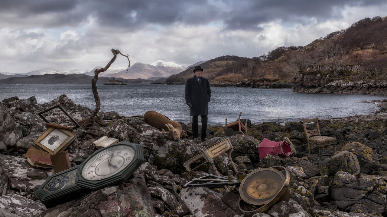 A man stands on a rocky, garbage strewn shore.