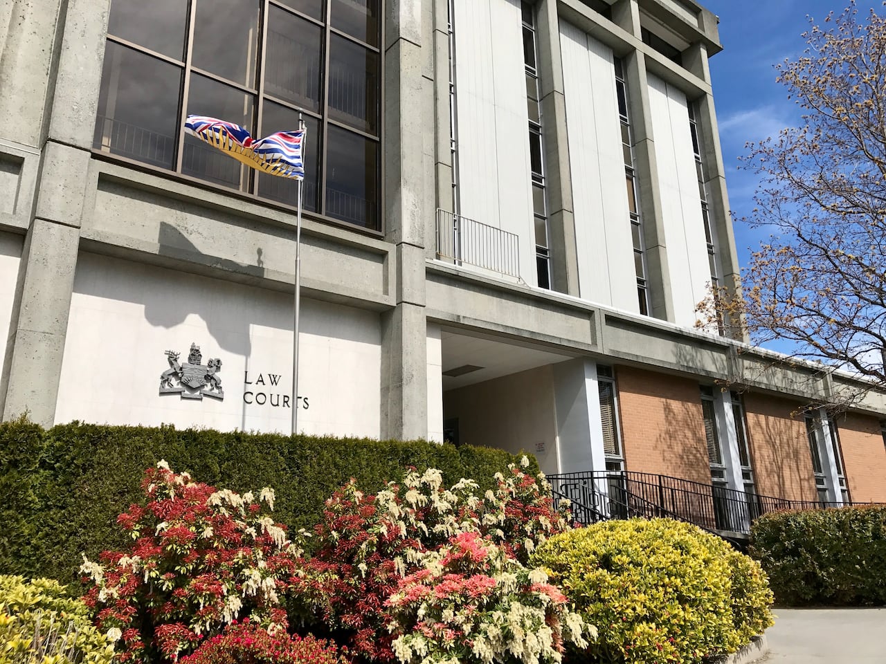 Victoria Law Courts is seen on a sunny day with a bush of flowers in front of it.