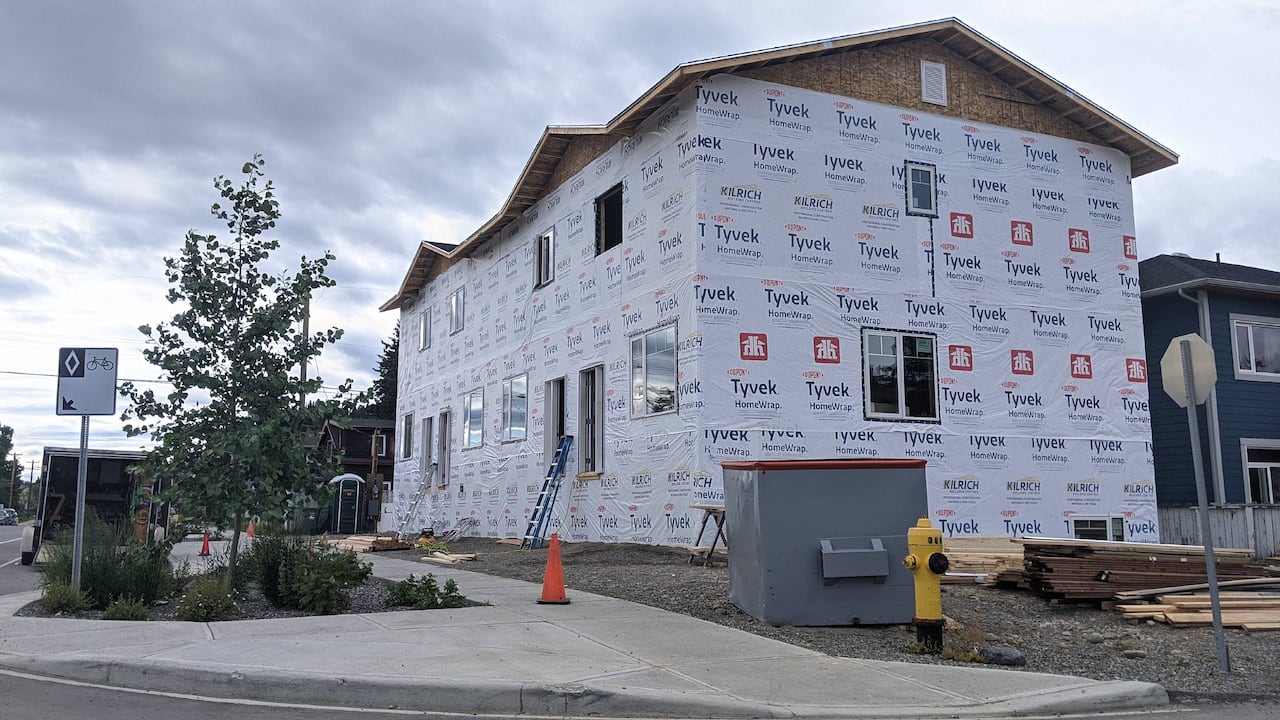 A large, two-level housing complex under construction, covered in Tyvek vapour barrier. 